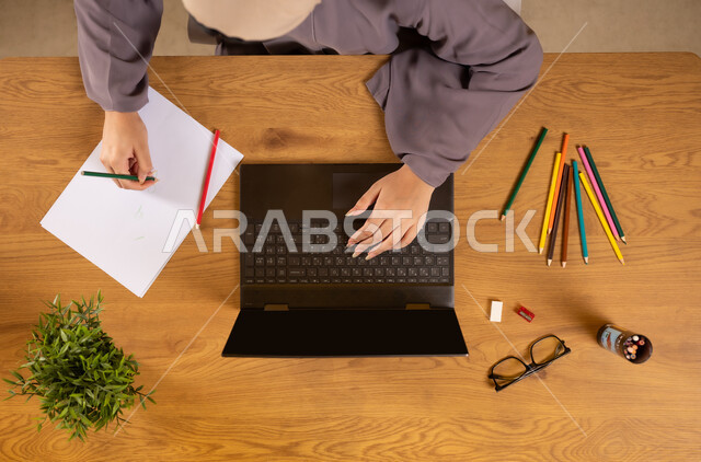 Interest in activities and hobbies, learning and training through websites, practicing the talent of drawing and coloring, a vertical upper portrait of an Arab Gulf Omani woman using a laptop and drawing distinctive artistic designs, enjoying handicrafts, using modern technology