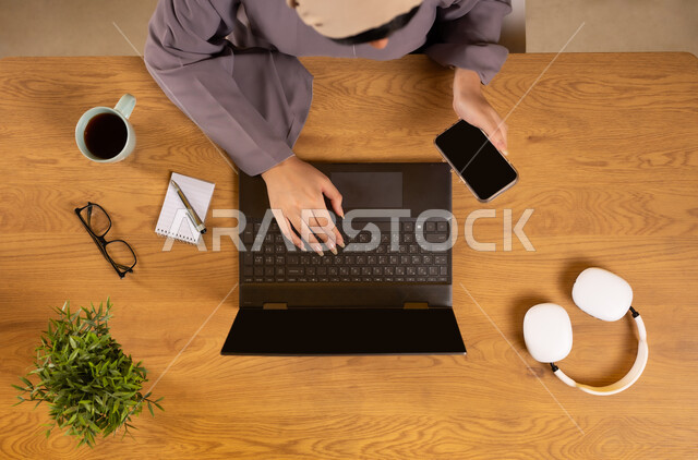 تسوق وسائل استماع الموسيقى عبر المواقع الالكترونية، مفهوم الترفيه والتسلية بالأجهزة والتقنيات الحديثة والمتطورة، دمج التكنولوجيا في الحياة اليومية، بورتريه علوي عامودي لإمرأة عربية خليجية عمانية تستخدم الهاتف والحاسوب المحمول، عرض شاشة سوداء فارغة