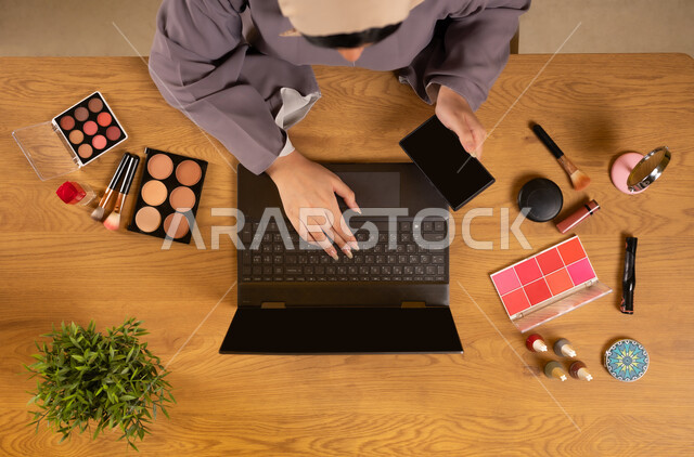 دمج التكنولوجيا والتقنيات الحديثة في الحياة اليومية، مفهوم الأنوثة والاهتمام بالجمال والمظهر الخارجي، أدوات تجميل نسائية عصرية، التسويق لمكياج وميكاب تتوريال، بورتريه علوي عامودي لإمرأة عربية خليجية عمانية تستخدم الهاتف والحاسوب المحمول، عرض شاشة سوداء فارغة