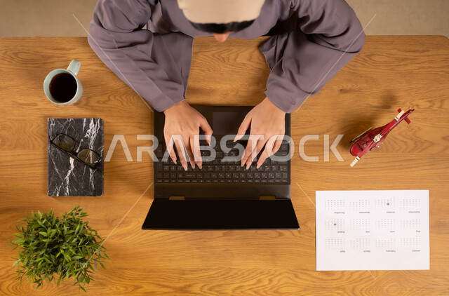 الحصول على المستلزمات اللازمة عن طريق الاونلاين، الاستعداد لقضاء رحلة صيفية ممتعة، مفهوم السياحة والقيام بالجولات الترفيهية، بورتريه علوي عامودي لإمرأة عربية خليجية عمانية تستخدم جهاز الحاسوب المحمول، دمج التكنولوجيا في الحياة العملية