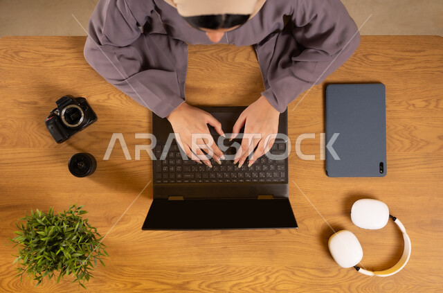 Using modern and advanced technologies, vertical overhead portrait of an Omani Gulf Arab woman using a laptop, integrating technology into daily life, training through the internet, obtaining the necessary supplies through the internet, shopping through electronic websites