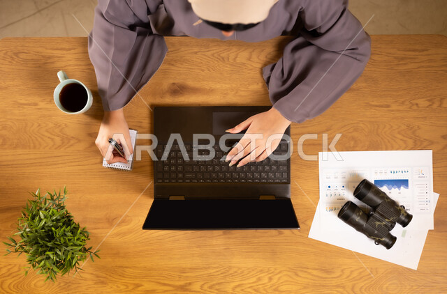 تدوين الملاحظات على الدفتر، مراقبة الإقتصاد والمعلومات المالية، دمج الأجهزة التقنية الحديثة بالحياة العملية، متابعة مخطط الرسوم البيانية، الإستثمار المالي الإلكتروني، بورتريه علوي عامودي لإمرأة عربية خليجية عمانية تقوم بدراسة وتحليل الإحصائيات عبر جهاز الحاسوب