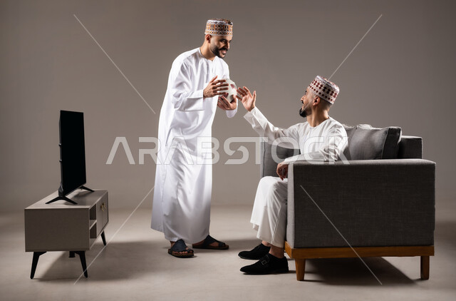 التفاعل والاندماج بمشاهدة الفريق المفضل, المباريات والالعاب الرياضية, بورتريه لرجلان عربيان عمانين خليجيان يرتديان الدشداشة والكمة احدهما يقف بإيماءات الحماس و الفوز والانتصار، الشغف بالانشطة الترفيهية, خلفية رمادية