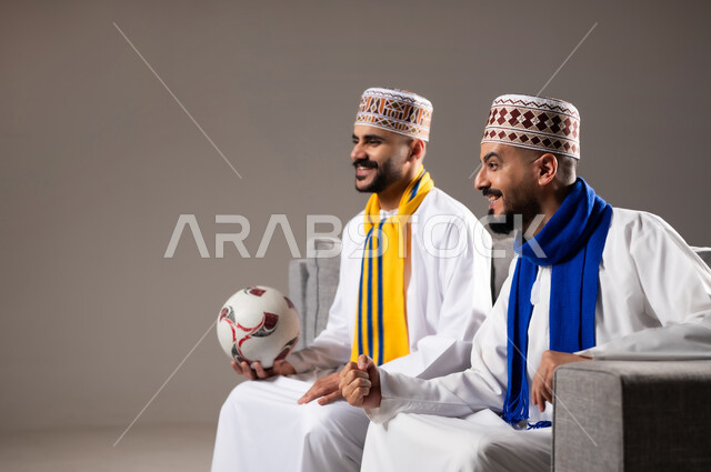 المباريات والالعاب الرياضية, التفاعل والاندماج بمشاهدة الفريق المفضل, ايماءات الفرح والحماس بالفوز والانتصار, بورتريه لرجلان عربيان عمانين خليجيان يرتديان الدشداشة والكمة احدهما يمسك بيده كرة قدم, الشغف بالانشطة الترفيهية, خلفية رمادية