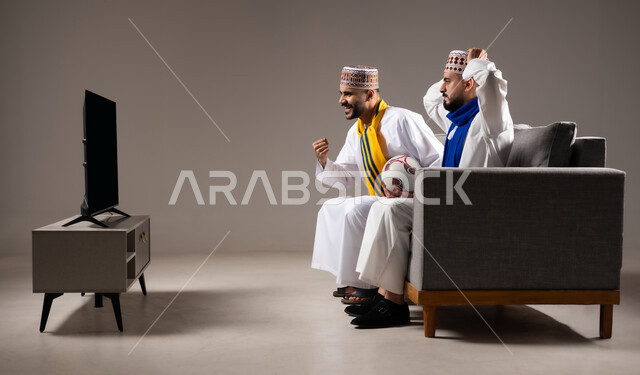 المباريات والالعاب الرياضية, التفاعل والاندماج بمشاهدة الفريق المفضل, ايماءات الفرح والحماس بالفوز والانتصار, بورتريه لرجلان عربيان عمانين خليجيان يرتديان الدشداشة والكمة احدهما يمسك بيده كرة قدم, الشغف بالانشطة الترفيهية, خلفية رمادية