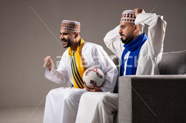 المباريات والالعاب الرياضية, التفاعل والاندماج بمشاهدة الفريق المفضل, ايماءات الفرح والحماس بالفوز والانتصار, بورتريه لرجلان عربيان عمانين خليجيان يرتديان الدشداشة والكمة احدهما يمسك بيده كرة قدم, الشغف بالانشطة الترفيهية, خلفية رمادية