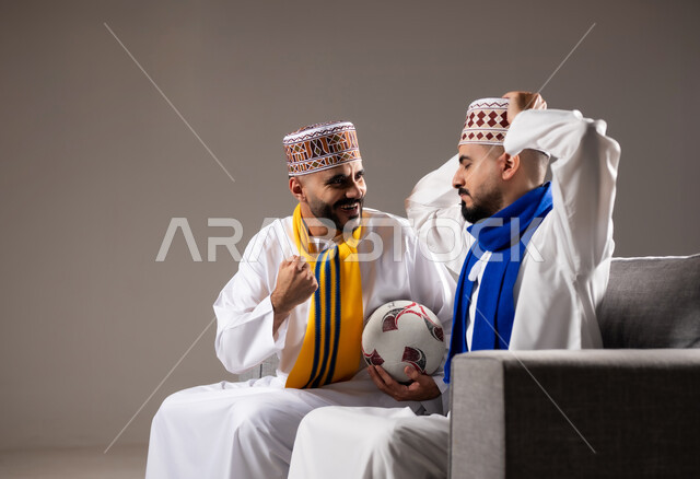 المباريات والالعاب الرياضية, التفاعل والاندماج بمشاهدة الفريق المفضل, ايماءات الفرح والحماس بالفوز والانتصار, بورتريه لرجلان عربيان عمانين خليجيان يرتديان الدشداشة والكمة احدهما يمسك بيده كرة قدم, الشغف بالانشطة الترفيهية, خلفية رمادية
