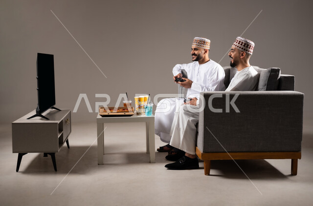 تناول الوجبات السريعة والمشاريب المنعشة, التفاعل والاندماج بمشاهدة الفريق المفضل, المباريات والالعاب الرياضية، بورتريه لرجلان عربيان عمانين خليجيان يرتديان الدشداشة والكمة احدهما يمسك بيده كرة قدم, الشغف بالانشطة الترفيهية, خلفية رمادية
