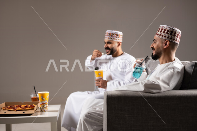 تناول الوجبات السريعة والمشاريب المنعشة, التفاعل والاندماج بمشاهدة الفريق المفضل, المباريات والالعاب الرياضية، بورتريه لرجلان عربيان عمانين خليجيان يرتديان الدشداشة والكمة احدهما يمسك بيده كرة قدم, الشغف بالانشطة الترفيهية, خلفية رمادية