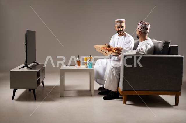 المباريات والالعاب الرياضية, تناول الوجبات السريعة والمشاريب المنعشة, بورتريه لرجلان عربيان عمانين خليجيان يرتديان الدشداشة والكمة احدهما يمسك قطعة من بيتزا, الشغف بالانشطة الترفيهية, خلفية رمادية
