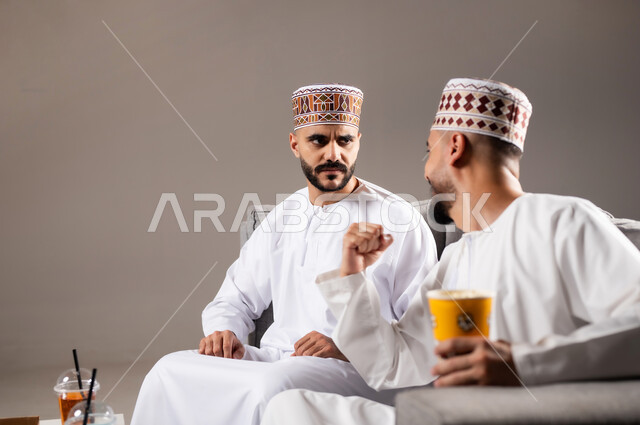 المباريات والالعاب الرياضية, تناول الوجبات السريعة والمشاريب المنعشة, التفاعل والاندماج بمشاهدة الفريق المفضل, ايماءات الفرح والحماس بالفوز والانتصار, بورتريه لرجلان عربيان عمانين خليجيان يرتديان الدشداشة والكمة, الشغف بالانشطة الترفيهية, خلفية رمادية