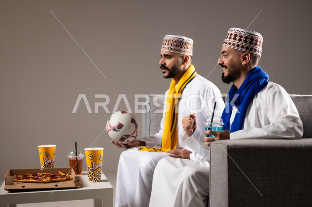 تناول الوجبات السريعة والمشاريب المنعشة, التفاعل والاندماج بمشاهدة الفريق المفضل, المباريات والالعاب الرياضية, ايماءات الفرح والحماس بالفوز والانتصار, بورتريه لرجلان عربيان عمانين خليجيان يرتديان الدشداشة والكمة احدهما يمسك بيده كرة قدم, الشغف بالانشطة الترفيهية, خلفية رمادية
