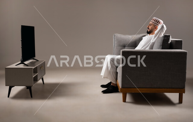 الشعور بالتعب والخمول والحاجة إلى النوم, إيماءات الراحة والإسترخاء، بورتريه لرجل عربي عماني خليجي يرتدي الدشداشة ويضع الكمة  يستريح على الكنبه, تعابير التأمل والتفكير، خلفية رمادية