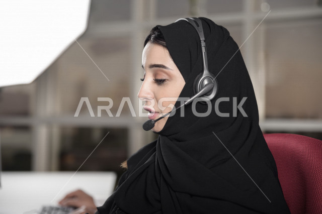 موظفة عربية خليجية سعودية تعمل في خدمة العملاء وتمسك الاوراق بيدها، موظفة ترتدي سماعة الاتصال، استعلامات واستفسارات، الاجابه على اسئلة العملاء، اجراء اتصال فيديو من خلال الحاسوب، متابعة وتطوير العمل