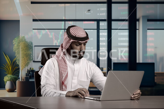 Integrating work with technology and technology, managing and organizing business affairs through technical devices, close-up image of a Saudi Arabian Gulf man wearing a traditional shemagh and thobe working on a laptop inside the company headquarters, administrative office jobs and professions in the Kingdom of Saudi Arabia