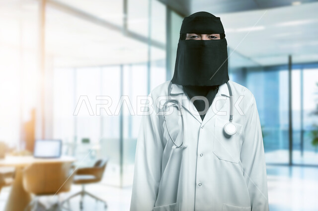 Providing medical services and examinations to patients, working in the health sector, close-up of a veiled Saudi Arabian Gulf female doctor wearing a white medical coat and niqab looking at the camera with gestures of self-confidence, women's professions and jobs in the Kingdom of Saudi Arabia