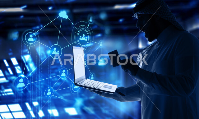 The concept of online electronic payment, using modern technologies, integrating advanced technology with work, a close-up image of a Saudi Arabian Gulf man wearing a traditional shemagh and thobe holding a laptop and a credit card, an electronic screen with illuminated holographic icons