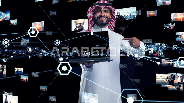 دمج التكنولوجيا المتطورة مع العمل، استخدام التقنيات الحديثة، رجل عربي خليجي سعودي يرتدي الشماغ والثوب التقليدي يشير باصبع السبابة الى جهاز اللابتوب المحمول ينظر الى الكاميرا بإيماءات الفرح والسرور، عناصر وشرائح هولوجرامية مضيئة، مفهوم التحول الرقمي