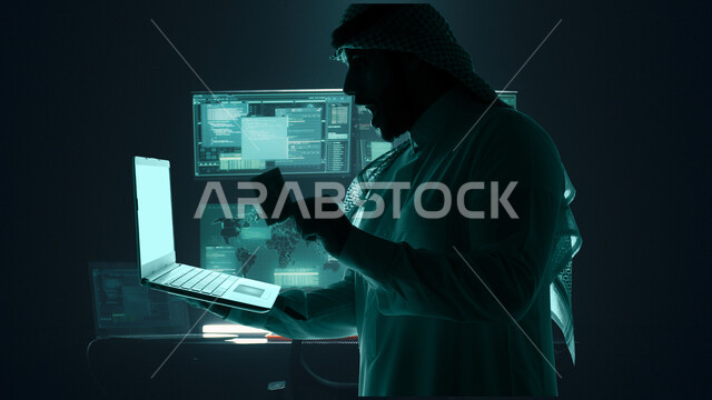 مفهوم الدفع الالكتروني عبر الانترنت، استخدام التقنيات الحديثة، دمج التكنولوجيا المتطورة مع العمل، صورة مقربة لرجل عربي خليجي سعودي يرتدي الشماغ والثوب التقليدي يمسك بيده جهاز اللابتوب المحمول وبطاقة ائتمان، شاشة إلكترونية بأيقونات هولوجرامية مضيئة