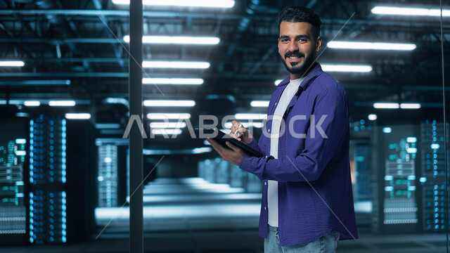 Using modern techniques and devices, integrating advanced technology with work, a Saudi Arabian Gulf man wearing a formal uniform holding a portable tablet in his hand, looking at the camera with gestures of self-confidence, success in achieving goals