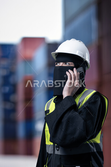 دمج التقنيات التكنولوجية بالمجال الهندسي، نهضة المجتمع السعودي بسواعد أبنائه، وظائف نسائية هندسية في المملكة, صورة مقربة لمهندسة عربية خليجية سعودية مسلمة منقبة ترتدي الخوذة البيضاء وسترة الحماية تمسك الهاتف المحمول تقوم بإجراء مكالمة هاتفية