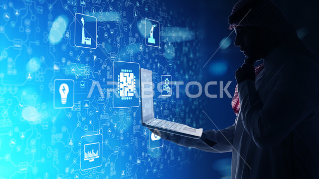 استخدام التقنيات الحديثة، دمج التكنولوجيا المتطورة مع العمل، صورة مقربة من الجانب لرجل عربي خليجي سعودي يرتدي الشماغ والثوب التقليدي يمسك بيده جهاز اللابتوب المحمول يقف امام شاشة إلكترونية بأيقونات هولوجرامية مضيئة، رؤية مستقبلية تكنولوجية، مفهوم التحول الرقمي