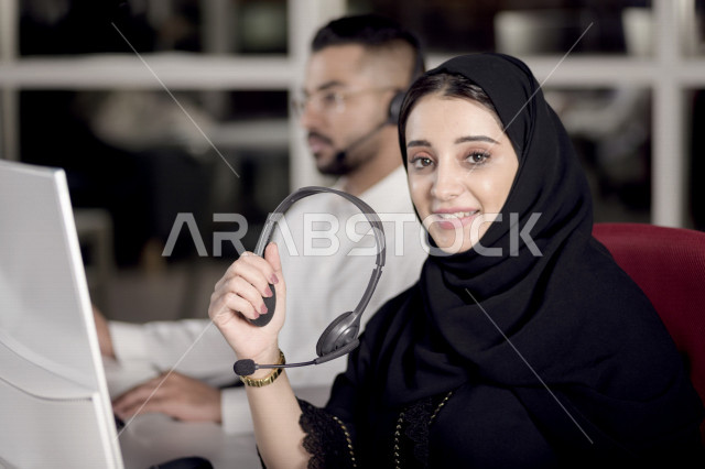 موظفان عربيان خليجيان سعوديان يعملان في خدمة العملاء، موظفة تمسك بيدها سماعة الاتصال، استعلامات واستفسارات، الاجابه على اسئلة العملاء، اجراء اتصال فيديو من خلال الحاسوب، متابعة وتطوير العمل