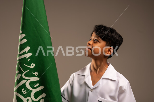 الفخر والإعتزاز لإمتلاك الهوية الوطنية، أهداف مستقبلية للوصول إلى مهنة طب الطوارئ، بورتريه مقرب لفتى عربي خليجي سعودي يرتدي زي التمريض ويحمل بيده علم المملكة، إحياء ذكرى العيد الوطني السعودي 23سبتمبر، يوم العلم 11مارس، خلفية رمادية