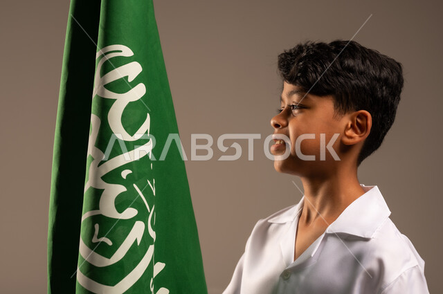 الفخر والإعتزاز لإمتلاك الهوية الوطنية، أهداف مستقبلية للوصول إلى مهنة طب الطوارئ، بورتريه مقرب لفتى عربي خليجي سعودي يرتدي زي التمريض ويحمل بيده علم المملكة، إحياء ذكرى العيد الوطني السعودي 23سبتمبر، يوم العلم 11مارس، خلفية رمادية