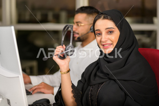 موظفان عربيان خليجيان سعوديان يعملان في خدمة العملاء، موظفة تمسك بيدها سماعة الاتصال، استعلامات واستفسارات، الاجابه على اسئلة العملاء، اجراء اتصال فيديو من خلال الحاسوب، متابعة وتطوير العمل