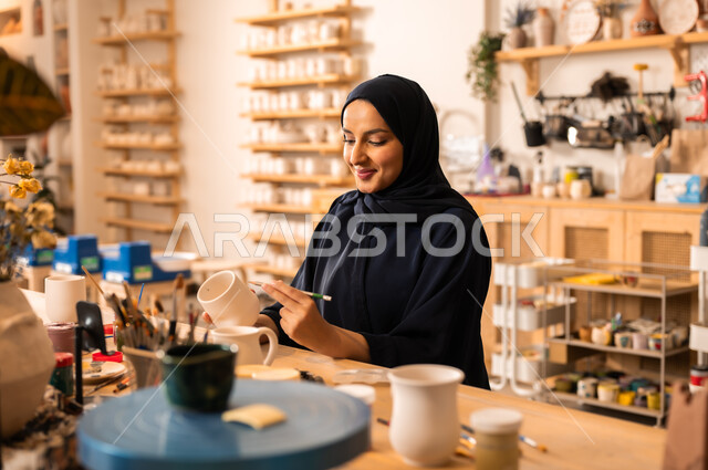  العمل في صناعة الخزفيات, تأسيس الدولة السعودية 1727 م, ذكرى اليوم الوطني السعودي23 سبتمبر, فن الرسم والتلوين على الخزف، امرأة عربية خليجية سعودية محجبة ترتدي العباءة السوداء تقوم بالرسم على السيراميك
