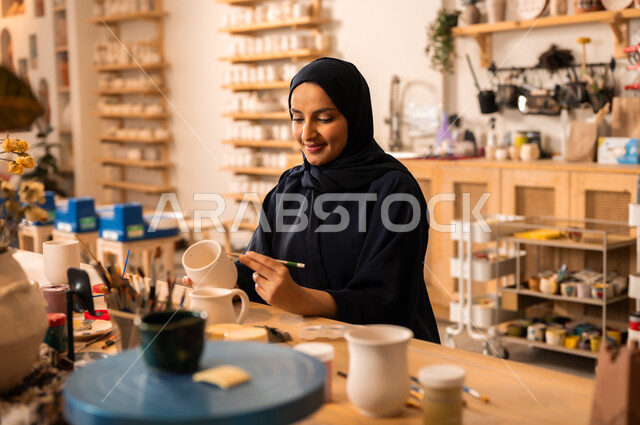  العمل في صناعة الخزفيات, تأسيس الدولة السعودية 1727 م, ذكرى اليوم الوطني السعودي23 سبتمبر, فن الرسم والتلوين على الخزف، امرأة عربية خليجية سعودية محجبة ترتدي العباءة السوداء تقوم بالرسم على السيراميك