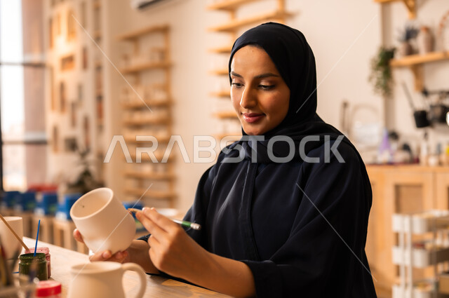  العمل في صناعة الخزفيات, تأسيس الدولة السعودية 1727 م, ذكرى اليوم الوطني السعودي23 سبتمبر, فن الرسم والتلوين على الخزف، امرأة عربية خليجية سعودية محجبة ترتدي العباءة السوداء تقوم بالرسم على السيراميك