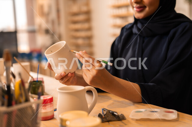  العمل في صناعة الخزفيات, تأسيس الدولة السعودية 1727 م, ذكرى اليوم الوطني السعودي23 سبتمبر, فن الرسم والتلوين على الخزف، امرأة عربية خليجية سعودية محجبة ترتدي العباءة السوداء تقوم بالرسم على السيراميك