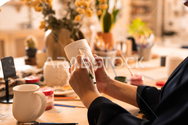  العمل في صناعة الخزفيات, تأسيس الدولة السعودية 1727 م, ذكرى اليوم الوطني السعودي23 سبتمبر, فن الرسم والتلوين على الخزف، امرأة عربية خليجية سعودية محجبة ترتدي العباءة السوداء تقوم بالرسم على السيراميك