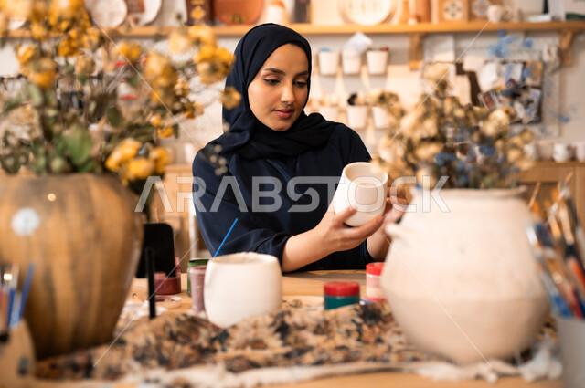  العمل في صناعة الخزفيات, تأسيس الدولة السعودية 1727 م, ذكرى اليوم الوطني السعودي23 سبتمبر, فن الرسم والتلوين على الخزف، امرأة عربية خليجية سعودية محجبة ترتدي العباءة السوداء تقوم بالرسم على السيراميك
