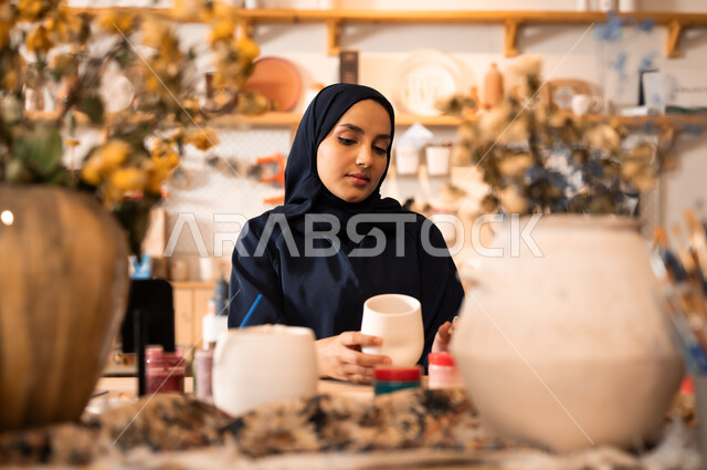  العمل في صناعة الخزفيات, تأسيس الدولة السعودية 1727 م, ذكرى اليوم الوطني السعودي23 سبتمبر, فن الرسم والتلوين على الخزف، امرأة عربية خليجية سعودية محجبة ترتدي العباءة السوداء تقوم بالرسم على السيراميك
