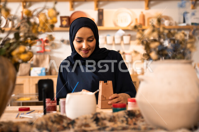 Pottery and clay products, the art of drawing and coloring on antiques, the founding of the Saudi state in 1727 AD, the anniversary of Saudi National Day September 23, a veiled Saudi Gulf Arab woman wearing a black abaya drawing on pottery