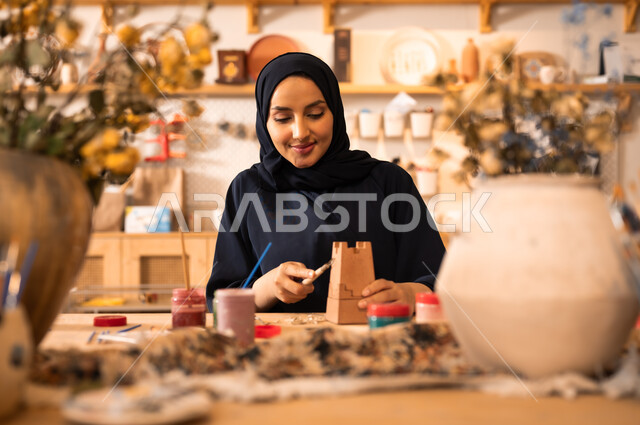  الأواني والمنتجات الفخارية المصنوعة من الطين, فن الرسم والتلوين على التحف, تأسيس الدولة السعودية 1727 م, ذكرى اليوم الوطني السعودي23 سبتمبر, امرأة عربية خليجية سعودية محجبة ترتدي العباءة السوداء تقوم بالرسم على الفخار