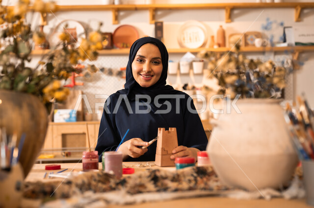  الأواني والمنتجات الفخارية المصنوعة من الطين, فن الرسم والتلوين على التحف, تأسيس الدولة السعودية 1727 م, ذكرى اليوم الوطني السعودي23 سبتمبر, امرأة عربية خليجية سعودية محجبة ترتدي العباءة السوداء تقوم بالرسم على الفخار
