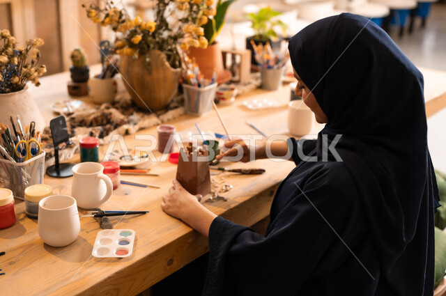 Pottery and clay products, the art of drawing and coloring on antiques, the founding of the Saudi state in 1727 AD, the anniversary of Saudi National Day September 23, a veiled Saudi Gulf Arab woman wearing a black abaya drawing on pottery
