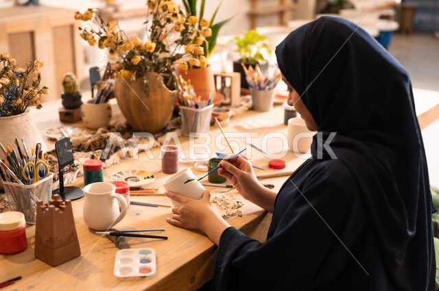  العمل في صناعة الخزفيات, تأسيس الدولة السعودية 1727 م, ذكرى اليوم الوطني السعودي23 سبتمبر, فن الرسم والتلوين على الخزف، امرأة عربية خليجية سعودية محجبة ترتدي العباءة السوداء تقوم بالرسم على السيراميك