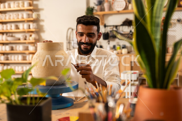 مناسبات واعياد وطنية, الصناعات التشكيلية اليدوية، شاب عربي خليجي سعودي يرتدي الثوب التقليدي يقوم برسم الزخرفة على جرة كبيرة, منحوتات وزخارف وأعمال فنية, حرف ومهن شعبية تراثية قديمة، تأسيس الدولة السعودية 1727 م, ذكرى اليوم الوطني السعودي 23 سبتمبر