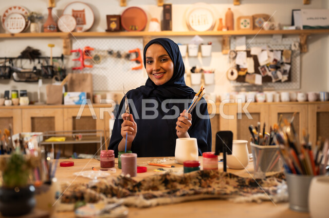  حرف ومهن شعبية تراثية قديمة, العمل في صناعة الخزفيات للاحتفال باليوم الوطني السعودي, امرأة عربية خليجية سعودية محجبة ترتدي العباءة السوداء تحمل بيدها معدات الرسم, إحياء ذكرى تأسيس الدولة السعودية 1727 م