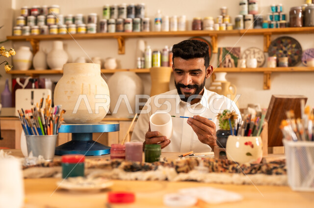 مناسبات واعياد وطنية, الصناعات التشكيلية اليدوية، شاب عربي خليجي سعودي يرتدي الثوب التقليدي يقوم بالرسم على السيراميك, منحوتات وزخارف وأعمال فنية, حرف ومهن شعبية تراثية قديمة، تأسيس الدولة السعودية 1727 م, ذكرى اليوم الوطني السعودي 23 سبتمبر