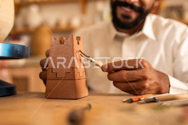 منحوتات وزخارف وأعمال فنية يدوية، حرف ومهن شعبية تراثية قديمة، تأسيس الدولة السعودية 1727 م, ذكرى اليوم الوطني السعودي 23 سبتمبر, الصناعات التشكيلية اليدوية، شاب عربي خليجي سعودي يرتدي الثوب التقليدي يقوم بالرسم على الفخار