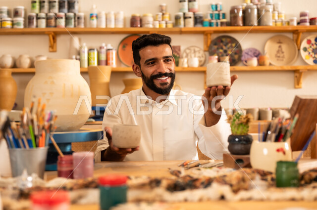 حرف ومهن شعبية تراثية قديمة، إحياء ذكرى تأسيس الدولة السعودية 1727 م, الاحتفال باليوم الوطني السعودي, شاب عربي خليجي سعودي يرتدي الثوب التقليدي يحمل بيديه الاعمال اليدوية