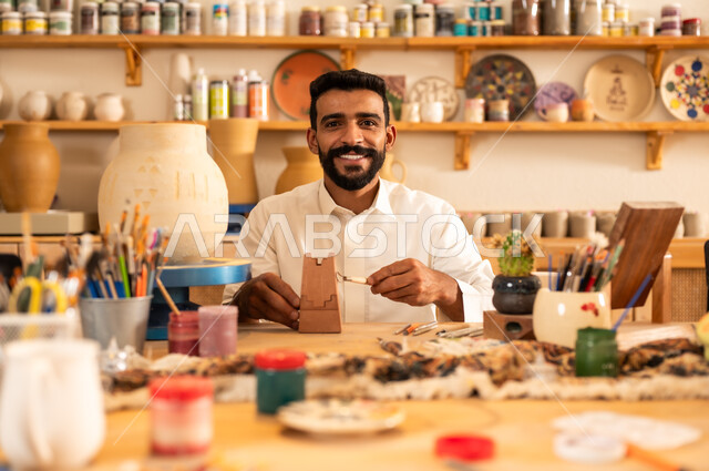 منحوتات وزخارف وأعمال فنية يدوية، حرف ومهن شعبية تراثية قديمة، تأسيس الدولة السعودية 1727 م, ذكرى اليوم الوطني السعودي 23 سبتمبر, الصناعات التشكيلية اليدوية، شاب عربي خليجي سعودي يرتدي الثوب التقليدي يقوم بالرسم على الفخار