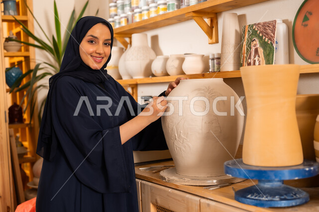  منحوتات وزخارف وأعمال فنية, الصناعات التشكيلية اليدوية, امرأة عربية خليجية سعودية محجبة ترتدي العباءة السوداء تقوم برسم الزخرفة على جرة كبيرة, حرف ومهن شعبية تراثية قديمة، تأسيس الدولة السعودية 1727 م, ذكرى اليوم الوطني السعودي 23 سبتمبر, مناسبات واعياد وطنية