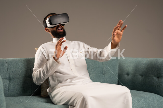 الاندماج ومحاكاة العالم الخيالي، الاستمتاع بمشاهدة أفلام الواقع الافتراضي، قضاء أوقات ممتعة ومسلية بالألعاب الافتراضية،  بورتريه لرجل عربي خليجي سعودي يرتدي الثوب التقليدي يجلس على كرسي مريح ويرتدي نظارة الواقع الافتراضي ثلاثية الابعاد، خلفية رمادية